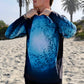 Angler 24-7 fishing shirt with fish design on beach.