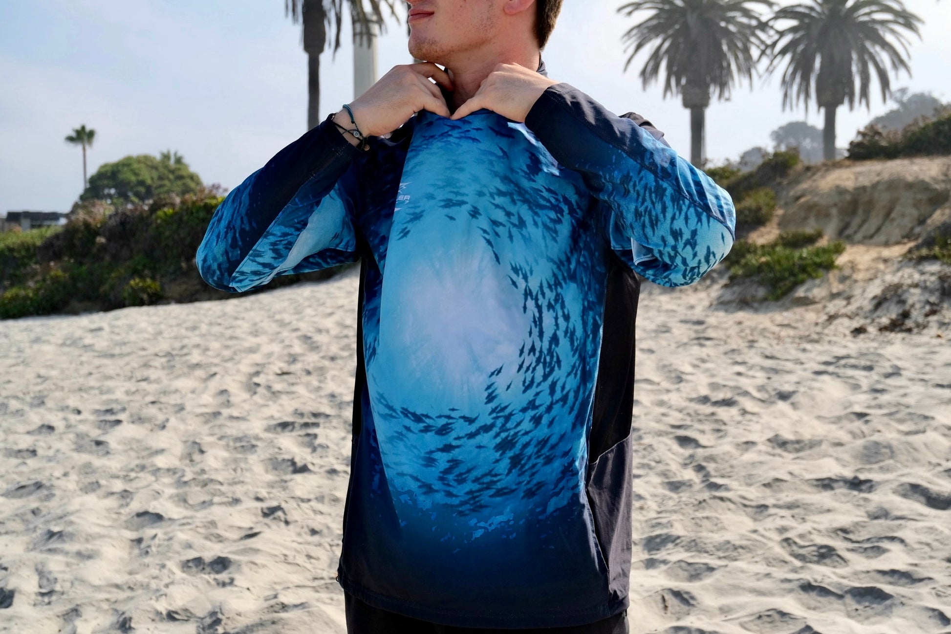 Angler 24-7 fishing shirt with fish design on beach.