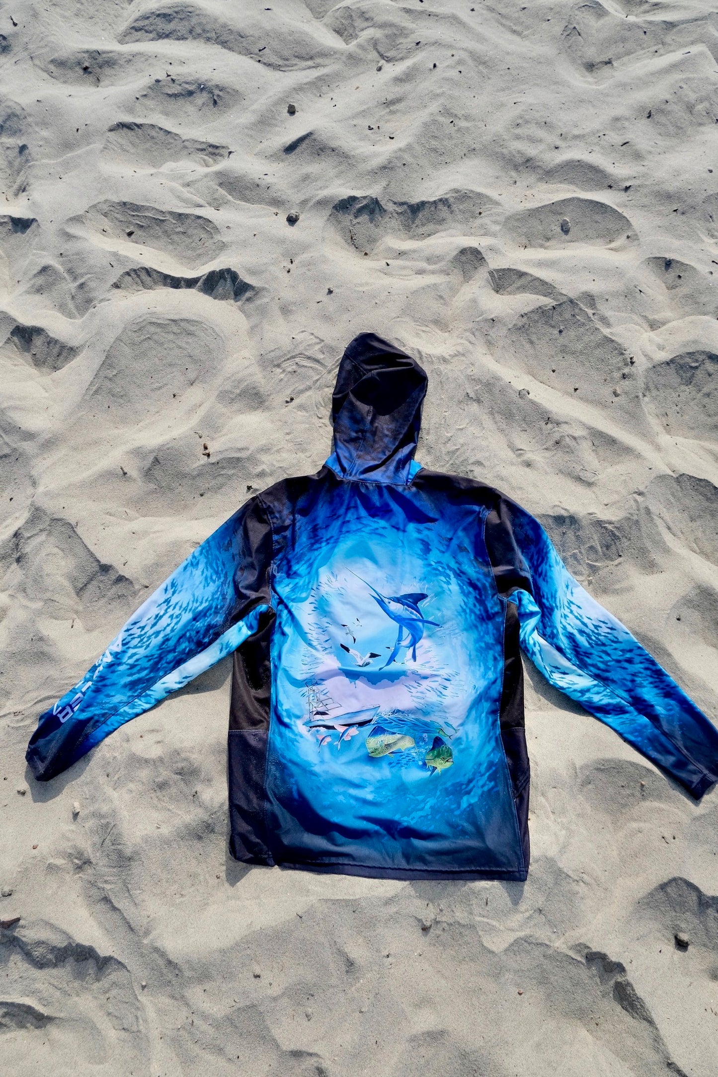 Angler 24-7 fishing shirt with fish design on sand.